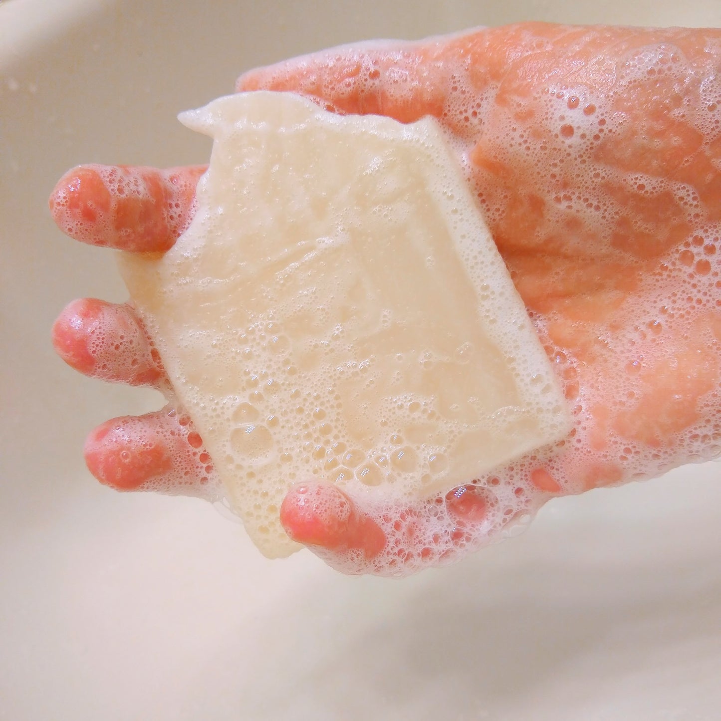 A hand cover with suds or bubbles holding a lathered bar of soap.