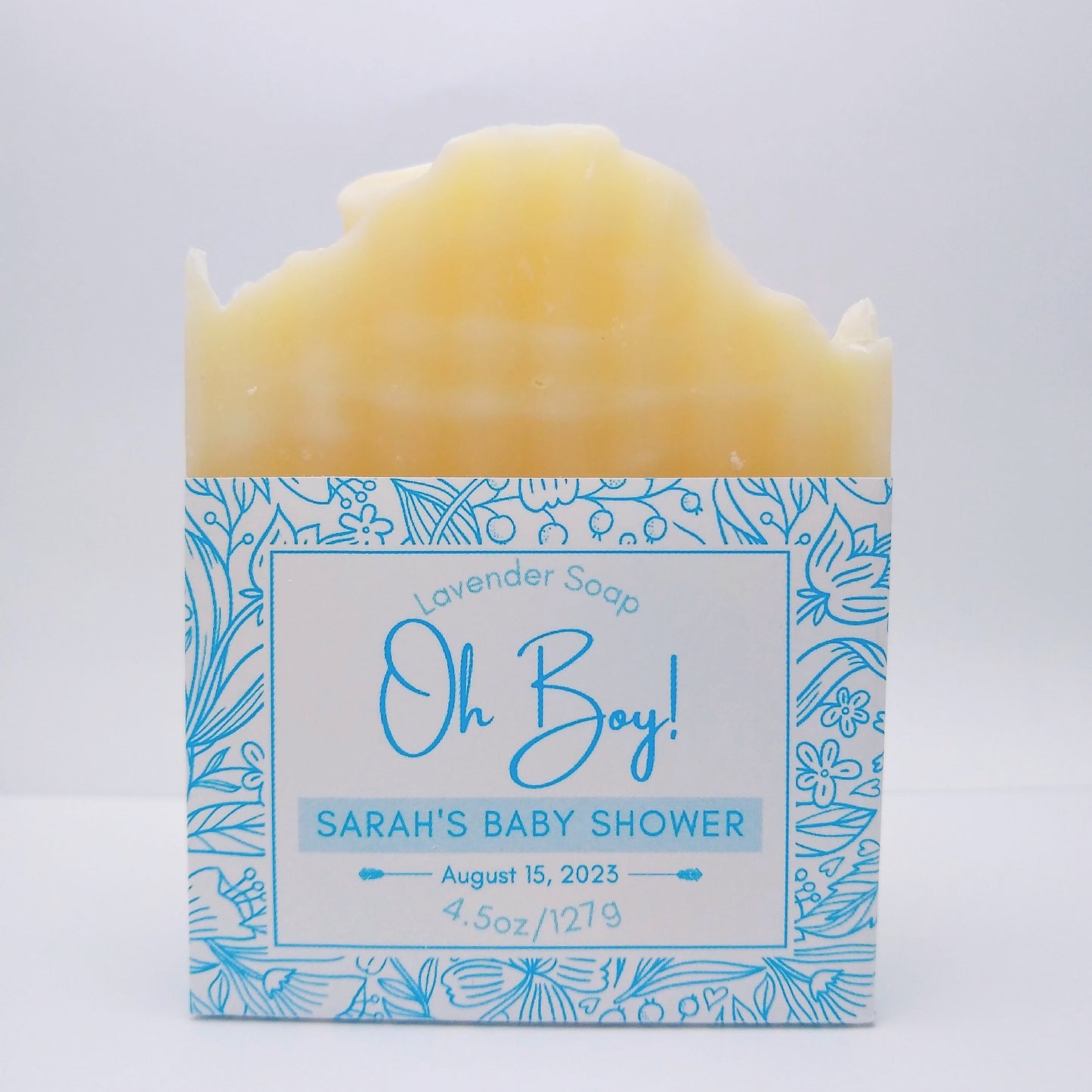 One bar of cream-colored soap with a blue label printed with "Oh Boy! Sarah's Baby Shower, August 15, 2023" and a flower-patterned accent around the border. 