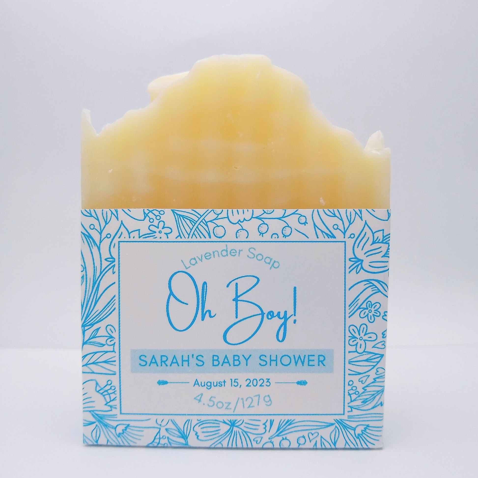 One bar of cream-colored soap with a blue label printed with "Oh Boy! Sarah's Baby Shower, August 15, 2023" and a flower-patterned accent around the border. 