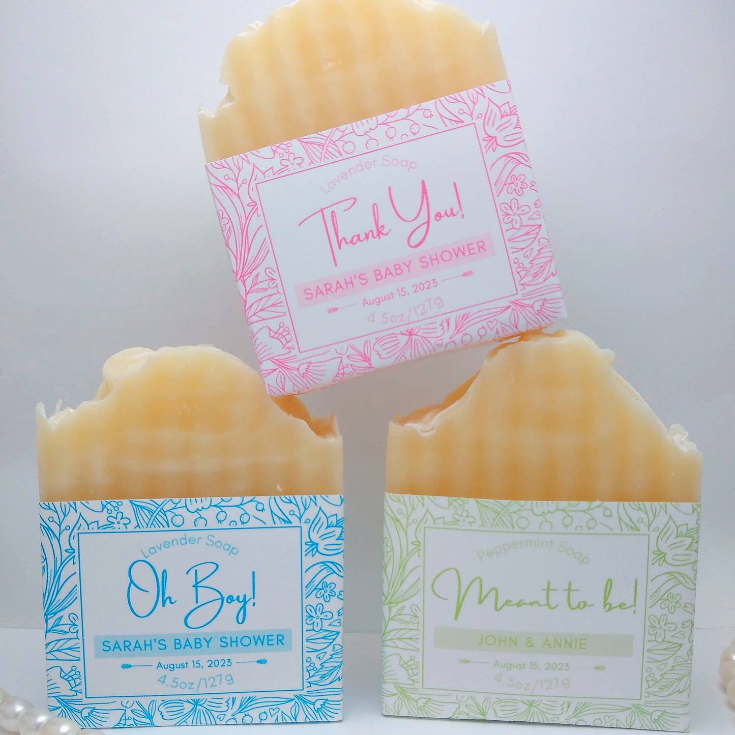 3 full bars of cream-colored soap with customized labels. One with a pink label saying "Thank you!", one with a blue label saying "Oh Boy!", and one with a light green label saying "Meant to Be". Each bar label is also printed with an event date.