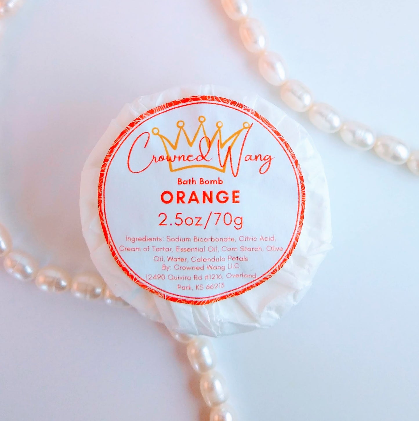 Crowned Wang brand 2.5oz orange bath bomb with orange and white label framed by pearls. The label also includes a yellow crown outline.